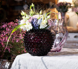Violet Hobnail Vase on a white fabric with vase in the background with colorful flowers