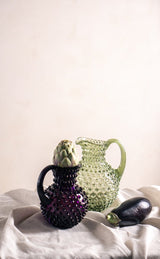 Violet Hobnail Jug Small on light grey fabric with artichoke and abergine as well as an off-white flond