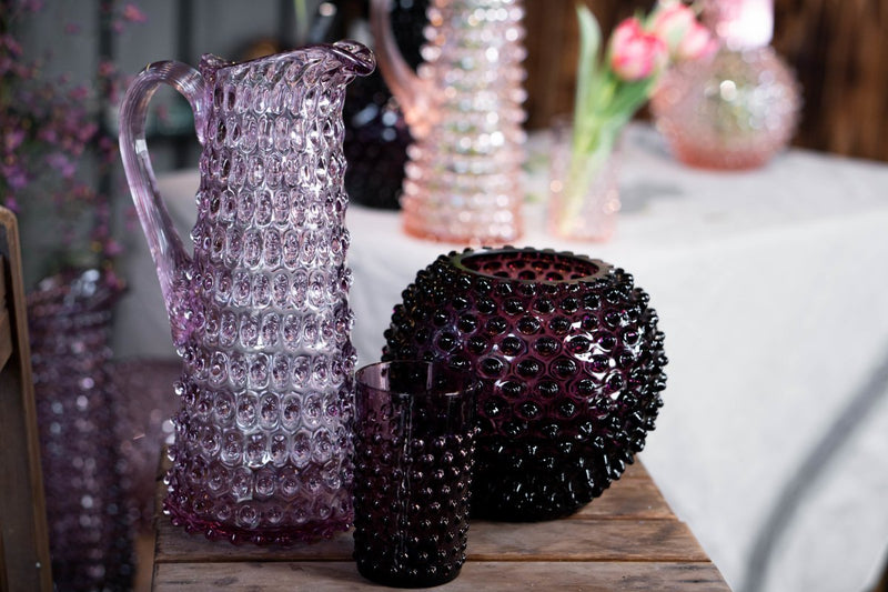 Violet Hobnail Vase on a wooden chair, surrounded by products from the Hobnail collection with colored flowers in the background