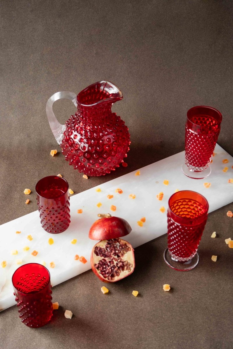 Underlay Garnet Hobnail Tumblers surrounded by products from the Hobnail collection and fruit on a black background 