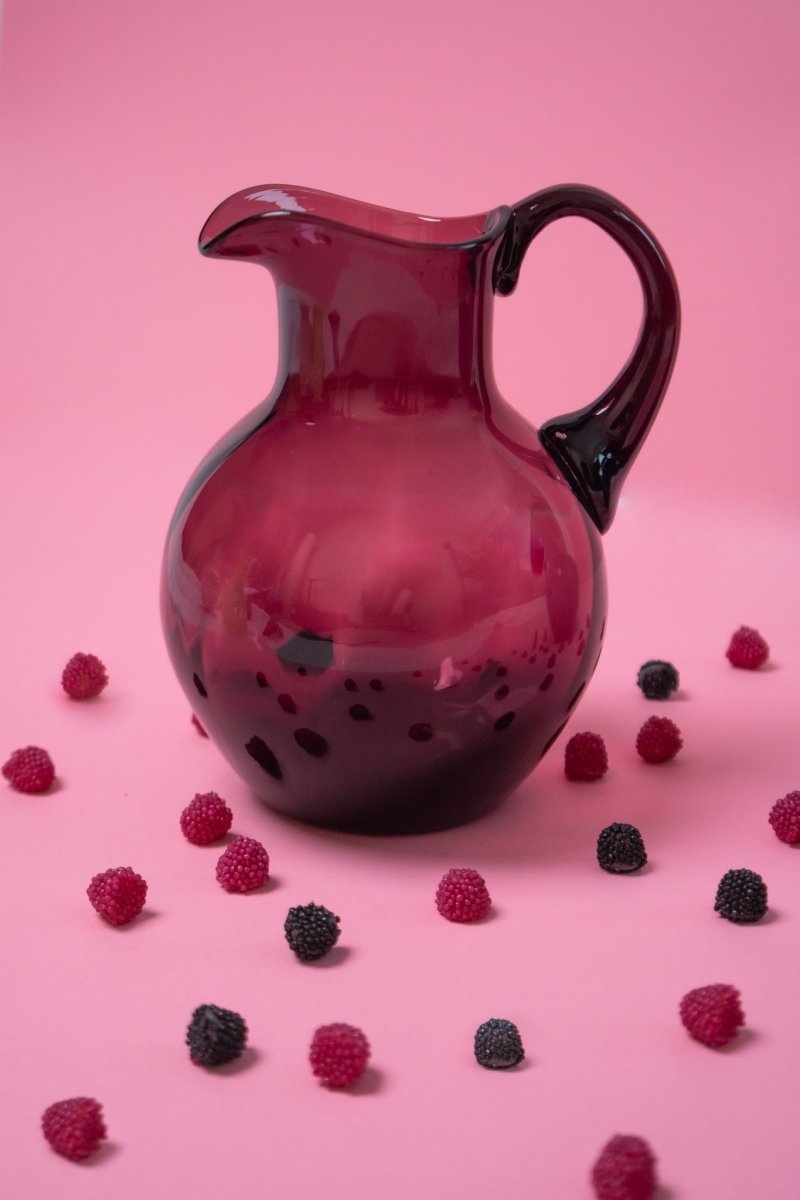 Violet Marika Jug surrounded by purple and black sweets on a pink background  