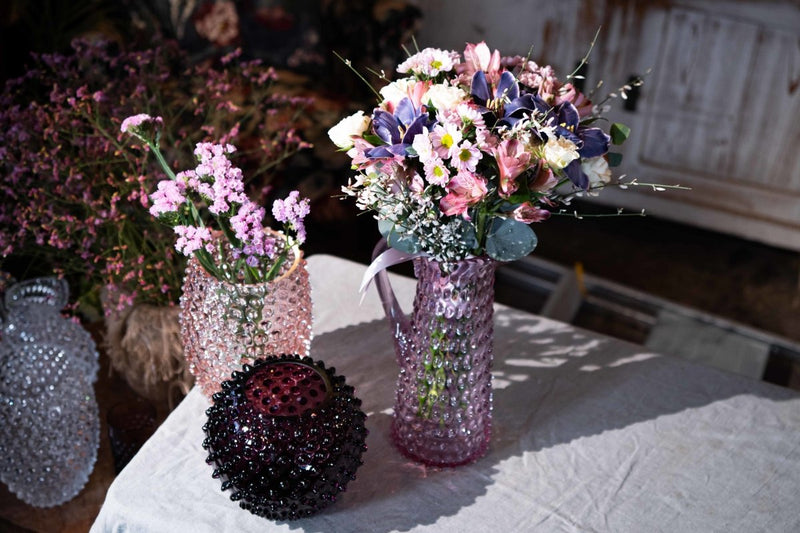 Violet Hobnail Vase on a white fabric surrounded by Hobnail product and colorful flowers