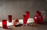 Underlay Garnet Hobnail Goblet (set of 2 pieces) surrounded by products from the Hobnail collection and fruit on a black background 