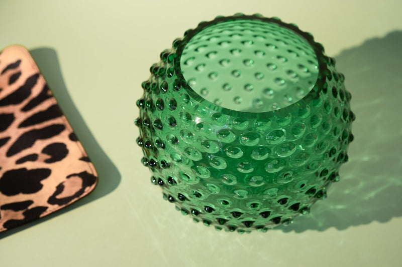 Underlay Dark Green Hobnail Vase with a leopard print pouch with an imitation leopard clutch on a white table 